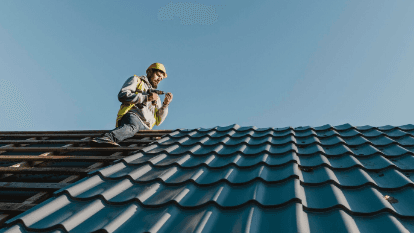 Roof inspector wearing a harness and hard hat following roofing safety standards while climbing a secured extension ladder