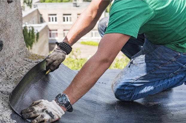 Homeowner clearing leaves from a gutter as part of routine roof maintenance.
