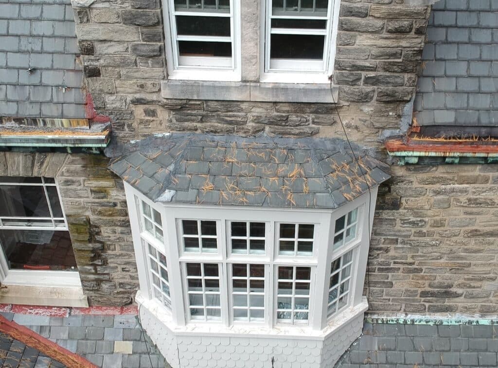 Oblique drone photograph of a slate roof showing corroded gutters, patched flashing and replaced shingles