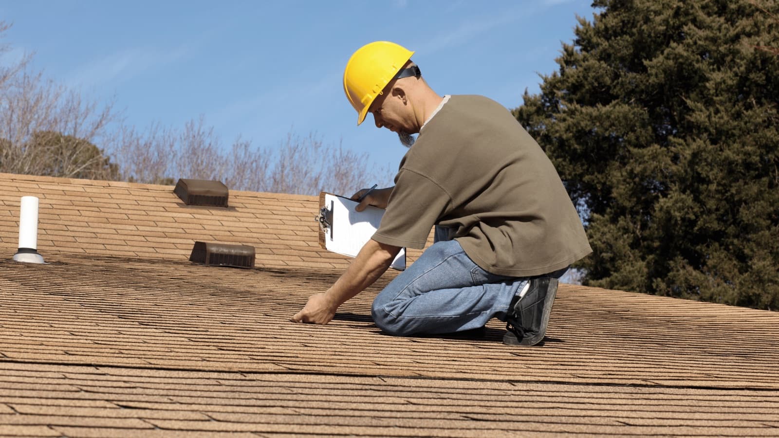 NRCIA inspector on an asphalt shingle roof documenting findings on a clipboard