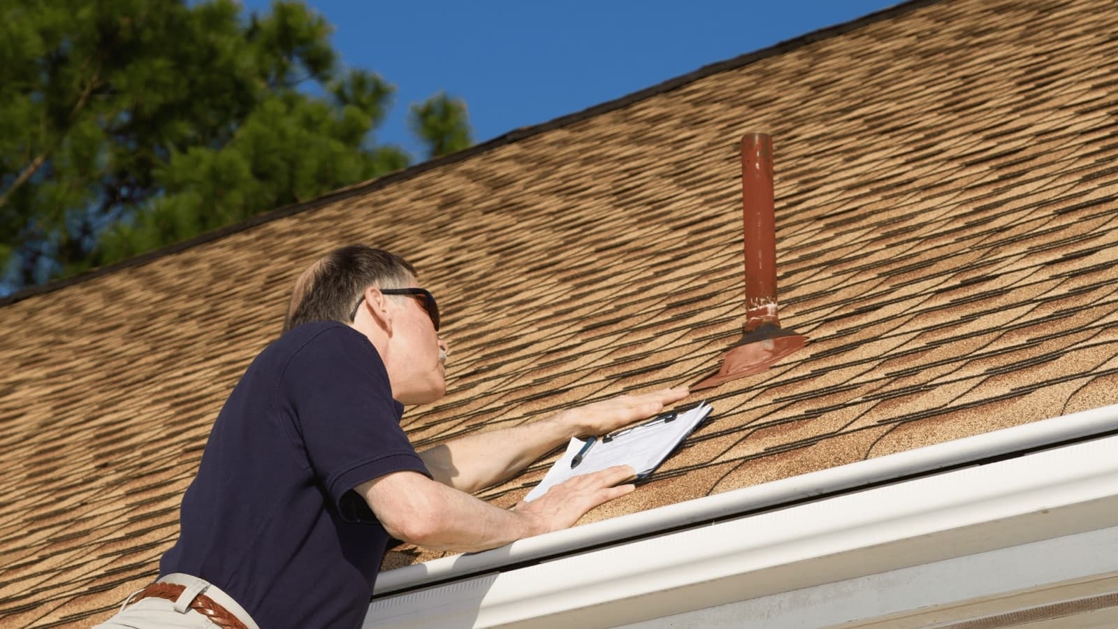 Roof inspector measuring attic insulation depth with a flashlight while checking roof energy efficiency