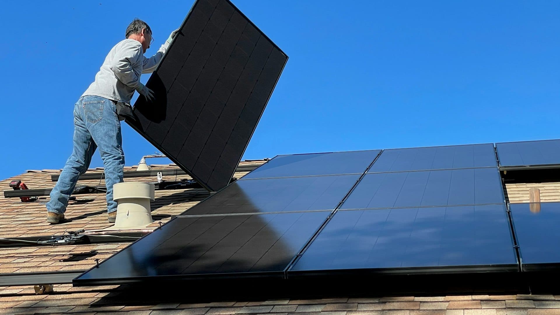 Installer placing a black solar panel onto an asphalt shingle roof