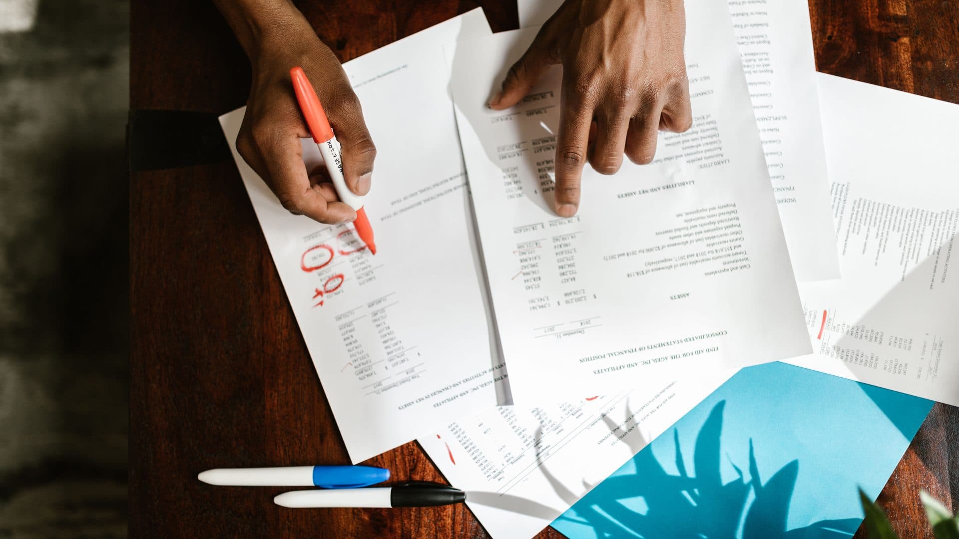 Hands marking up a printed report with a red pen on a desk