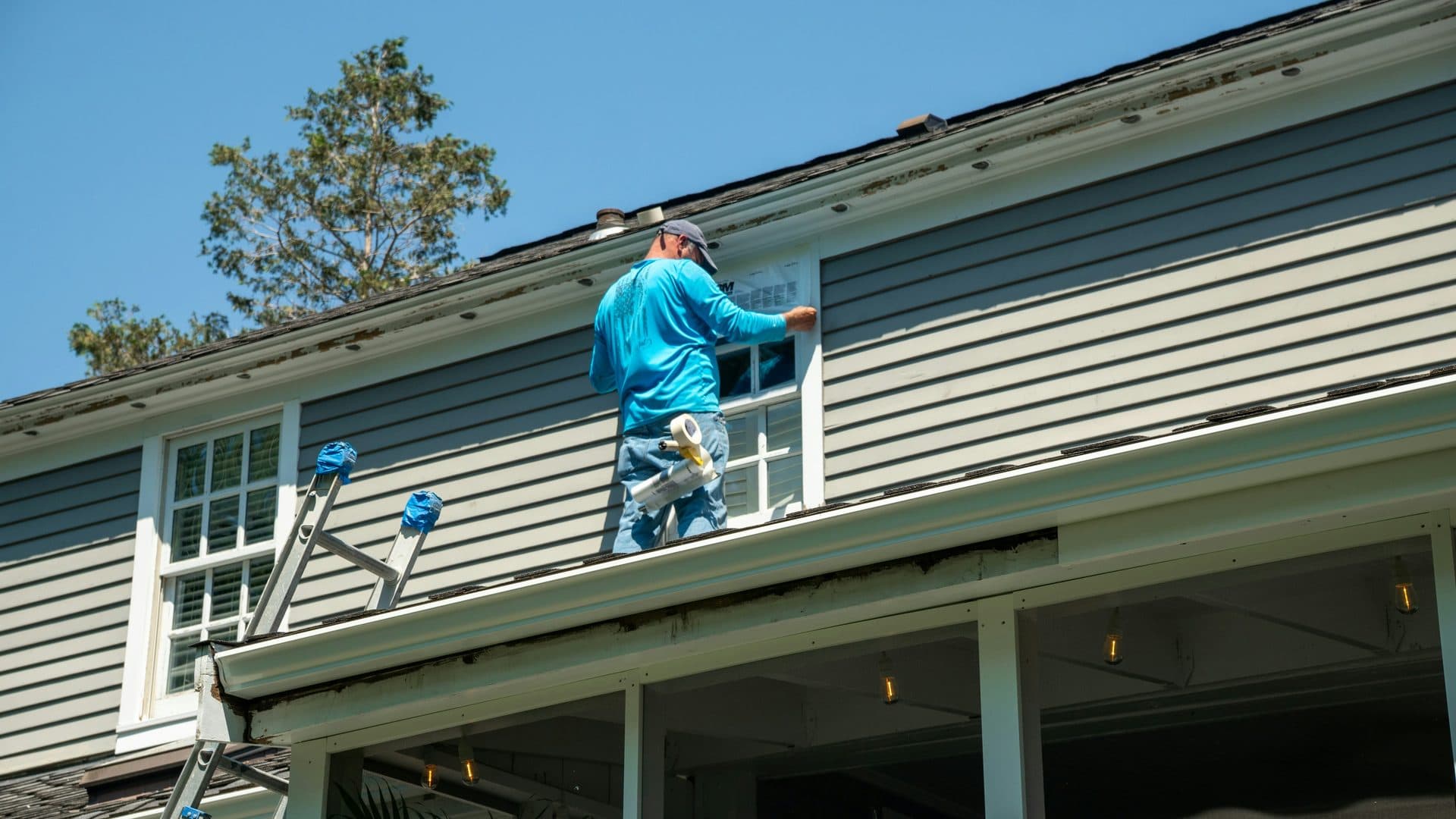 Worker on a lower roof where it meets the siding of a two-story wall