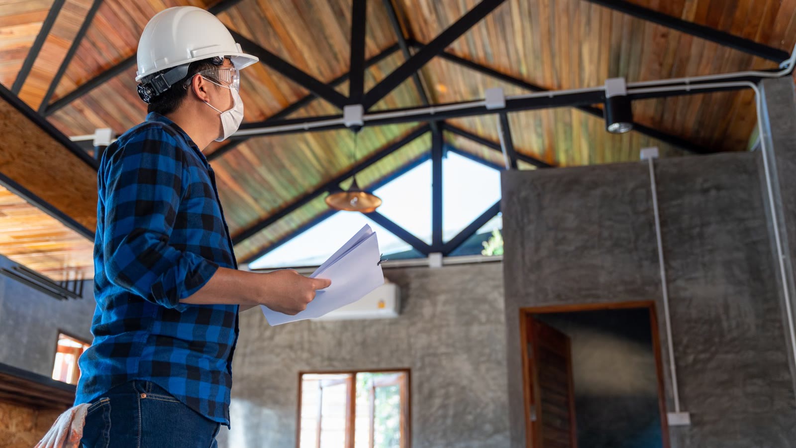Inspector in a hard hat checking a home's roof structure from inside